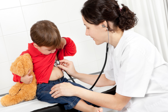 This image depicts a doctor with a stethoscope listening to a kid's heart. The kid is holding his teddy bear.  