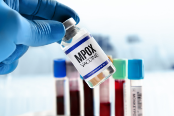 photo of a gloved hand holding a vial of Mpox vaccine