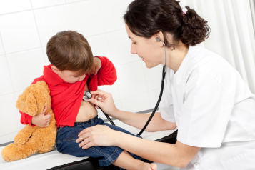 This image depicts a doctor with a stethoscope listening to a kid's heart. The kid is holding his teddy bear.  