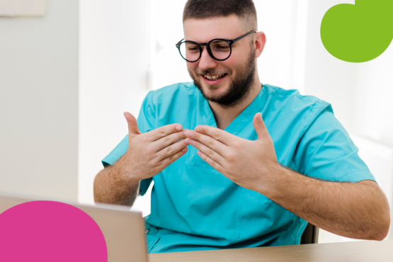 Photo of a man wearing blue scrubs, sitting at his desk, signing in BSL at his laptop screen. There is a stethoscope and a notebook on his desk. On the top right corner there is the Healthwatch logo. 