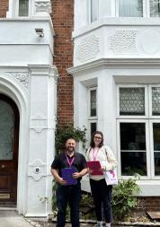 two healthwatch representatives pose outside the practice with their pink clipboards